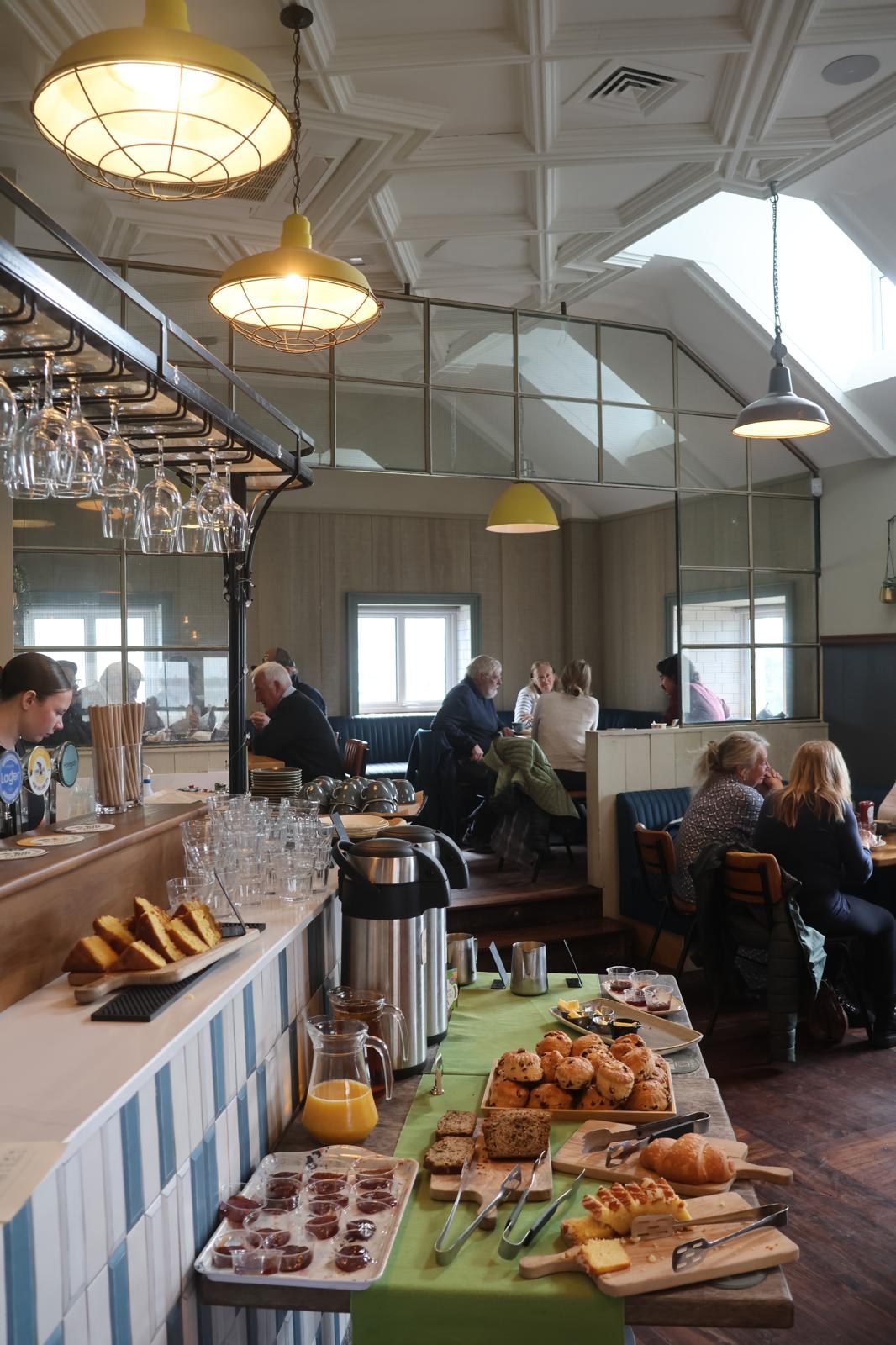 The breakfast buffet along the bar: scones, pastries, cake, jugs of orange juice and preserves, with members seated behind