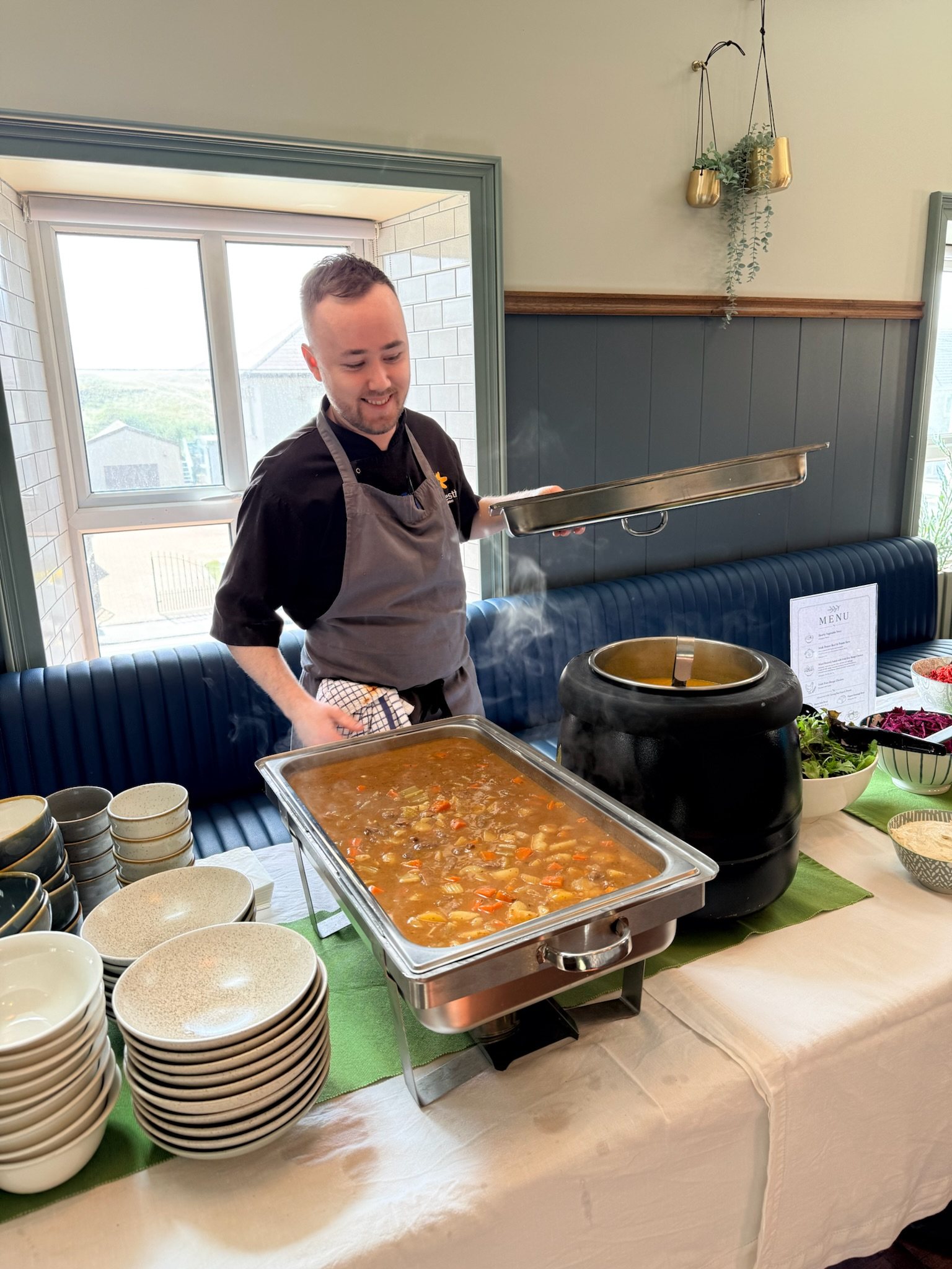 An Honestly chef lifting a tray of hot stew onto the buffet in the upstairs room at Strandhill
