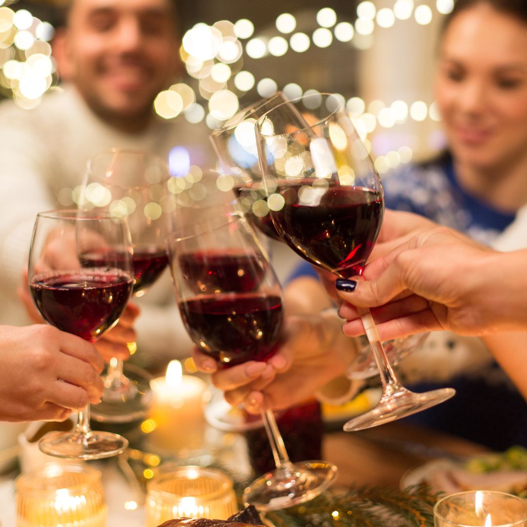 Friends raising glasses of red wine over a candlelit table, with fairy lights glowing behind
